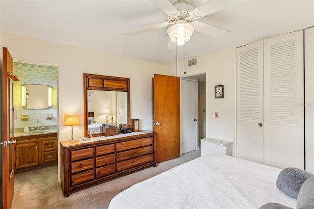 bedroom with a sink, a closet, ensuite bathroom, visible vents, and light colored carpet