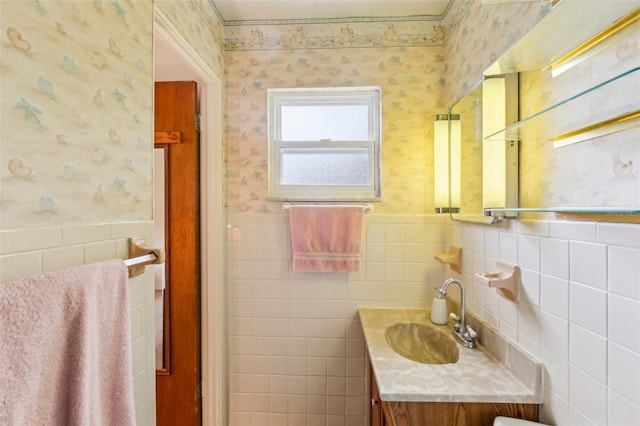 bathroom with tile walls, vanity, wallpapered walls, and a wainscoted wall