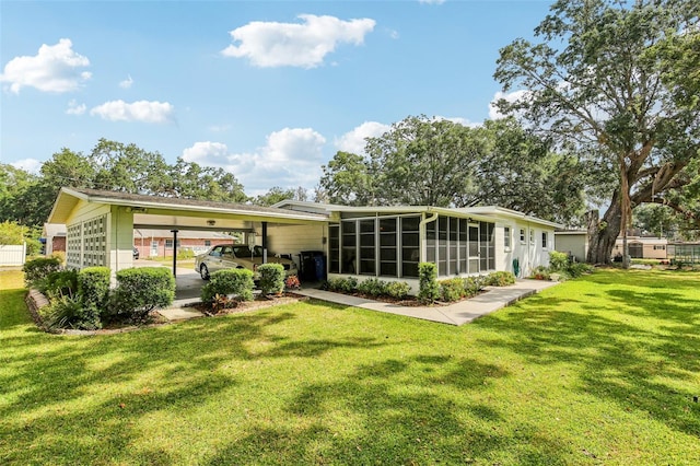 back of house featuring a sunroom, a lawn, and a carport
