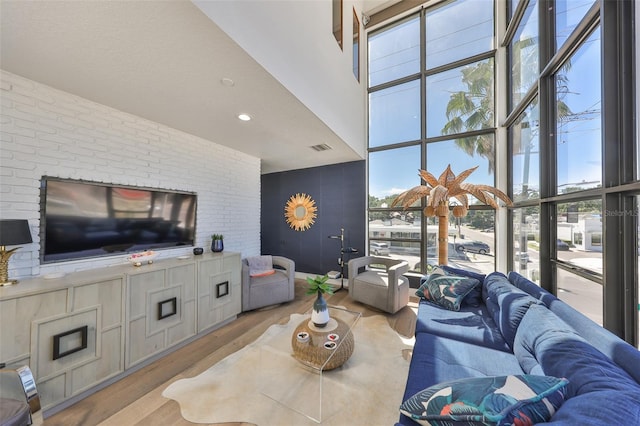 living room with a high ceiling, visible vents, a healthy amount of sunlight, and light wood-style floors
