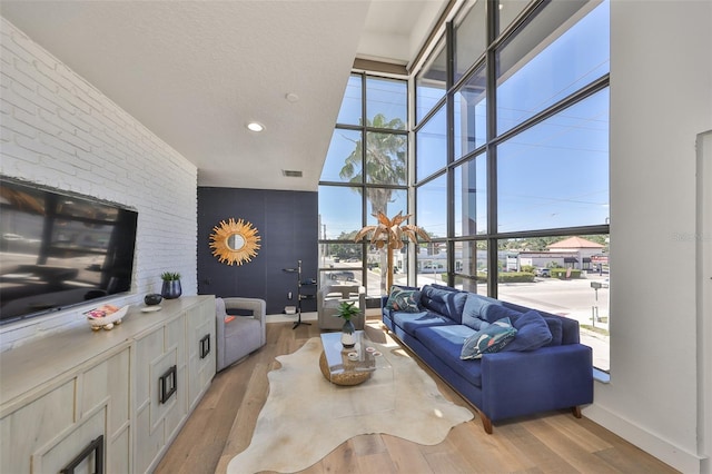 living area with floor to ceiling windows, visible vents, baseboards, a high ceiling, and light wood-style flooring