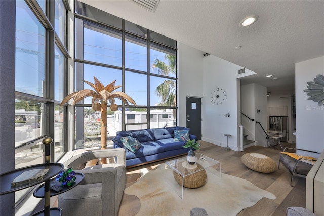 living room featuring a textured ceiling, visible vents, a towering ceiling, wood finished floors, and stairway