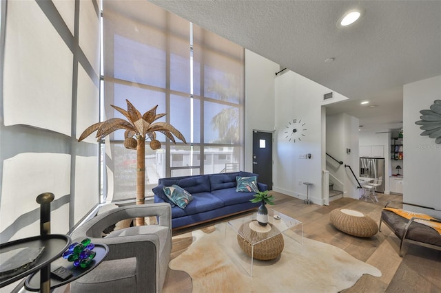 living area with visible vents, wood finished floors, baseboards, a high ceiling, and stairway