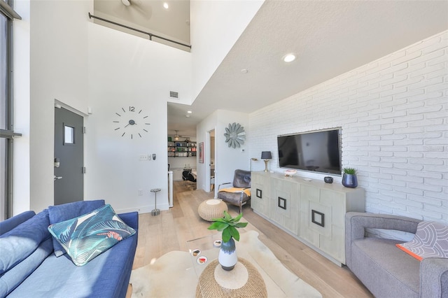 living area featuring light wood-type flooring, recessed lighting, a high ceiling, and brick wall