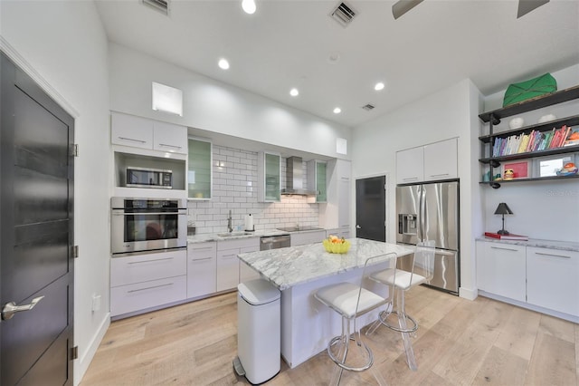kitchen featuring a kitchen bar, visible vents, a sink, stainless steel appliances, and wall chimney exhaust hood