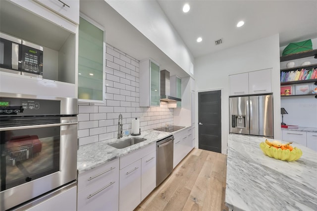 kitchen featuring wall chimney range hood, visible vents, light stone countertops, a sink, and stainless steel appliances