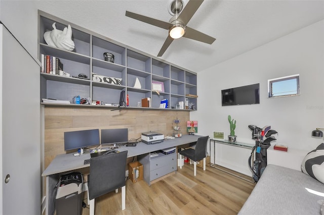 office space featuring a ceiling fan, built in desk, and wood finished floors