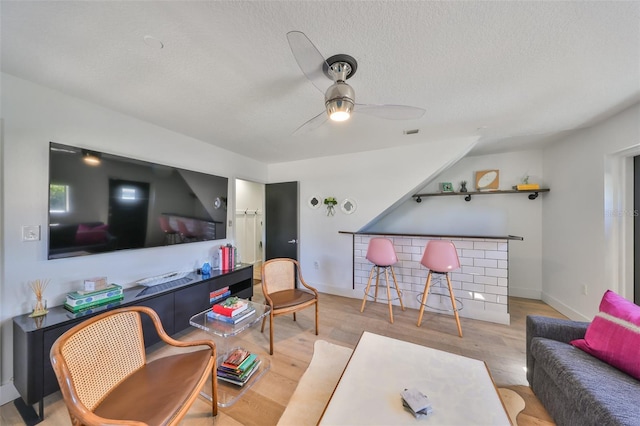 living room with a ceiling fan, a textured ceiling, visible vents, and wood finished floors