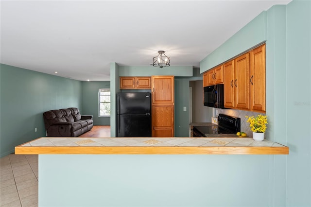 3353 Montano Ave, Spring Hill, FL 34609 - kitchen with a peninsula, tasteful backsplash, black appliances, tile counters, and light tile patterned floors