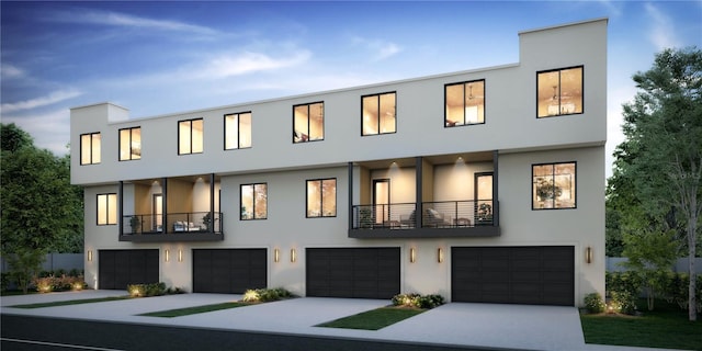 multi unit property with stucco siding, an attached garage, driveway, and a balcony