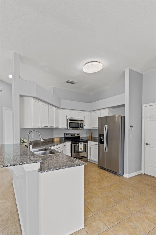 25830 Crippen Dr, Land O Lakes, FL 34639 - kitchen featuring appliances with stainless steel finishes, a peninsula, dark stone countertops, white cabinets, and light tile patterned floors