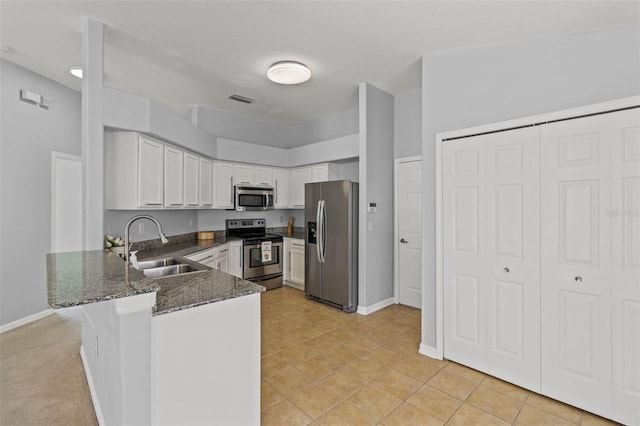 25830 Crippen Dr, Land O Lakes, FL 34639 - kitchen with stainless steel appliances, a peninsula, dark stone countertops, white cabinetry, and light tile patterned flooring
