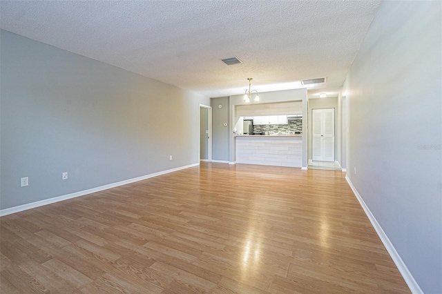 spare room featuring a textured ceiling, baseboards, visible vents, and light wood finished floors