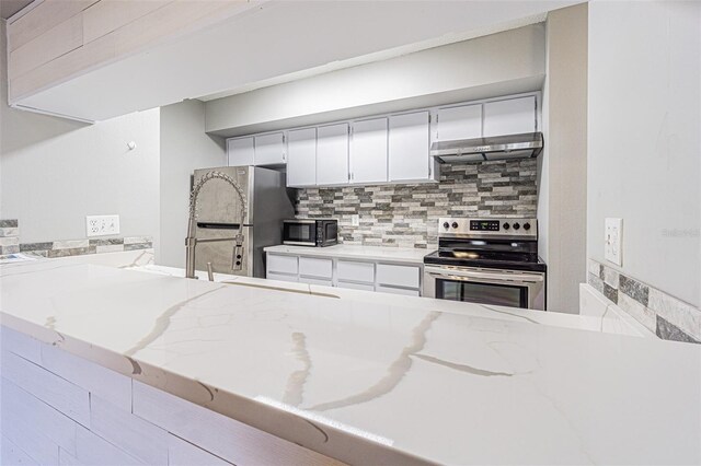 kitchen with light stone countertops, under cabinet range hood, white cabinets, appliances with stainless steel finishes, and backsplash