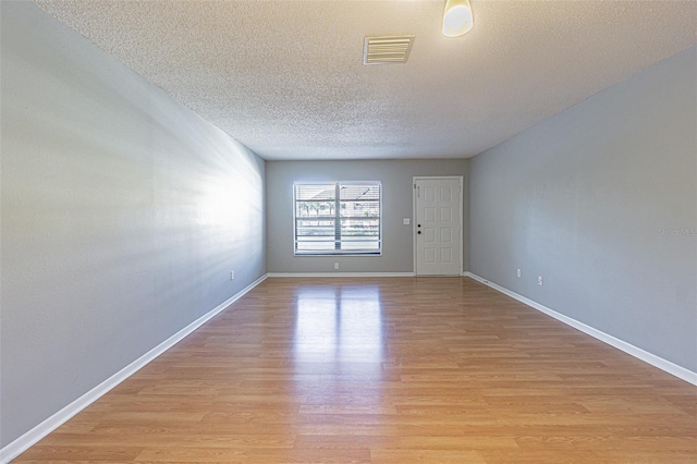 empty room featuring visible vents, a textured ceiling, light wood finished floors, and baseboards