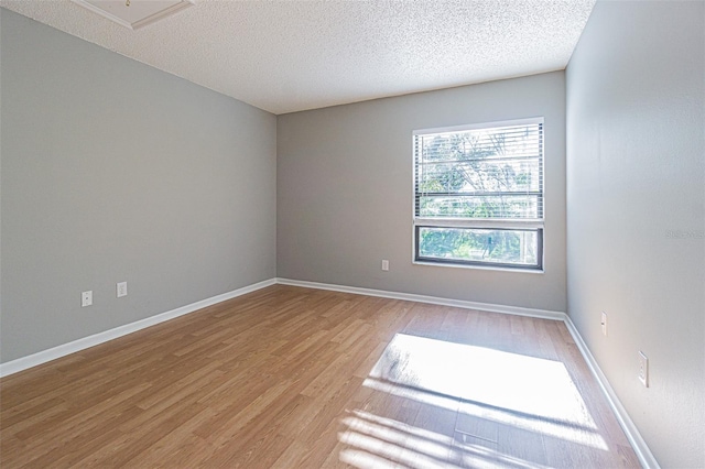 empty room featuring light wood-type flooring, a textured ceiling, and baseboards