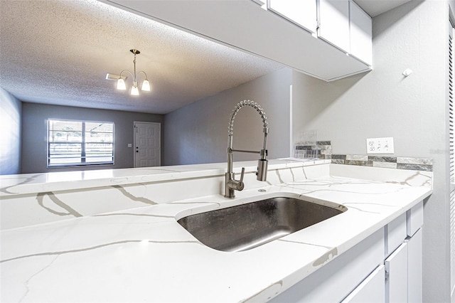 kitchen featuring a textured ceiling, hanging light fixtures, a sink, a chandelier, and white cabinetry
