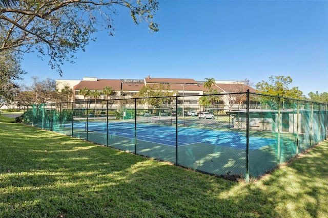 view of tennis court with a lawn and fence
