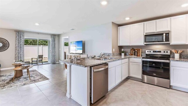 kitchen featuring appliances with stainless steel finishes, a sink, a peninsula, stone counters, and white cabinetry