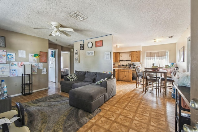 living area featuring a ceiling fan, a textured ceiling, and visible vents