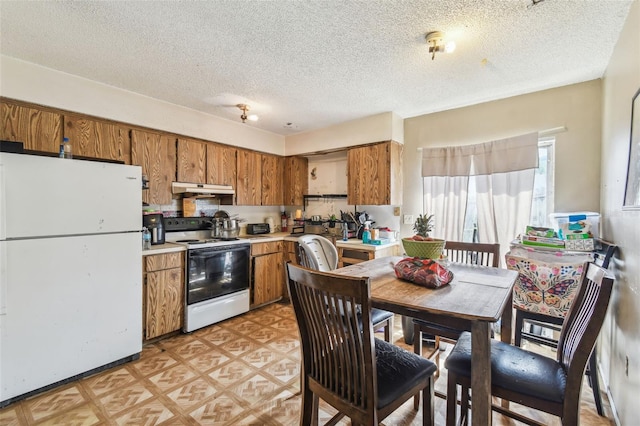 kitchen with white appliances, brown cabinets, under cabinet range hood, and light countertops