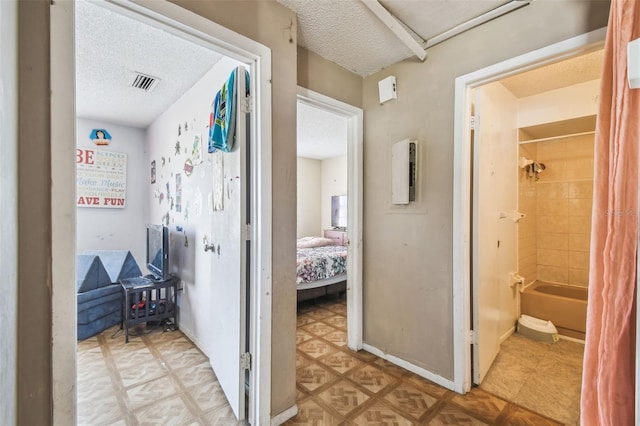 hallway with baseboards, a textured ceiling, and visible vents