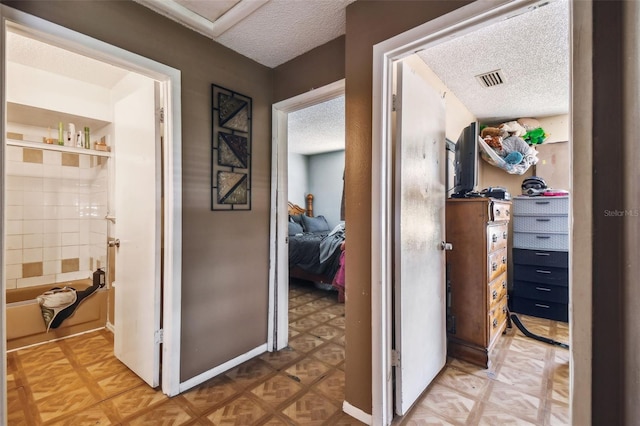 corridor featuring a textured ceiling, visible vents, baseboards, and light floors