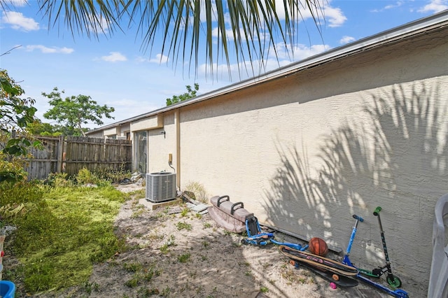 view of side of home featuring fence, cooling unit, and stucco siding