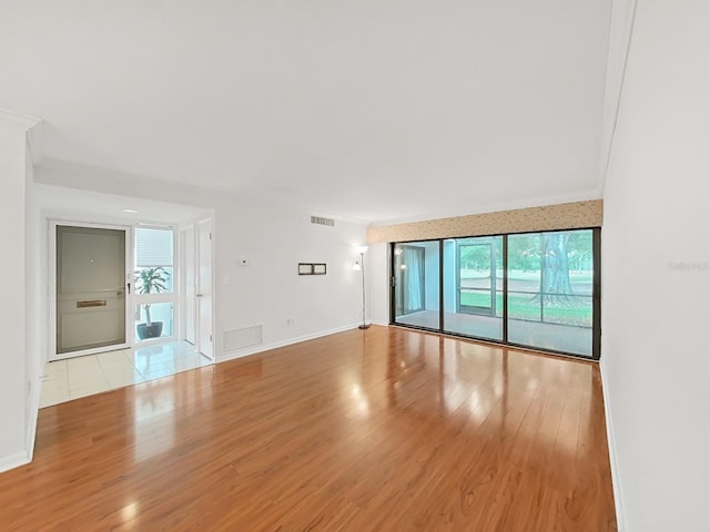 unfurnished living room featuring crown molding, baseboards, wood finished floors, and visible vents