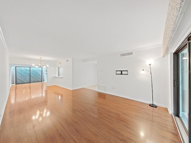 unfurnished living room featuring visible vents, light wood-style floors, baseboards, and an inviting chandelier