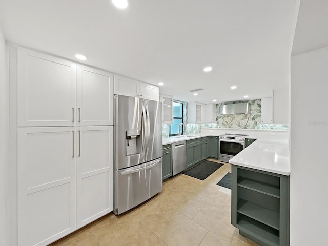kitchen featuring wall chimney range hood, light countertops, white cabinetry, a sink, and appliances with stainless steel finishes