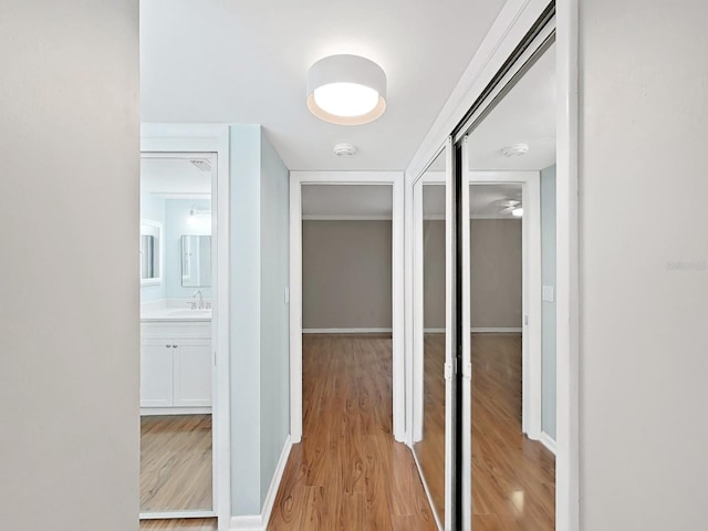 corridor featuring a sink, baseboards, and light wood-style flooring