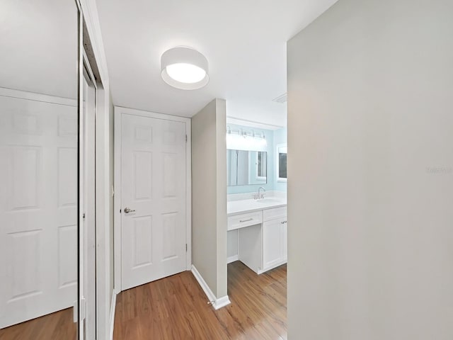 corridor with light wood-style floors, a sink, and baseboards