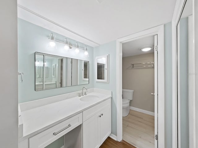 bathroom featuring vanity, baseboards, wood finished floors, and toilet