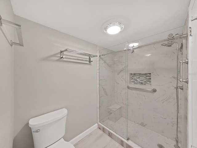 bathroom with baseboards, a marble finish shower, and toilet