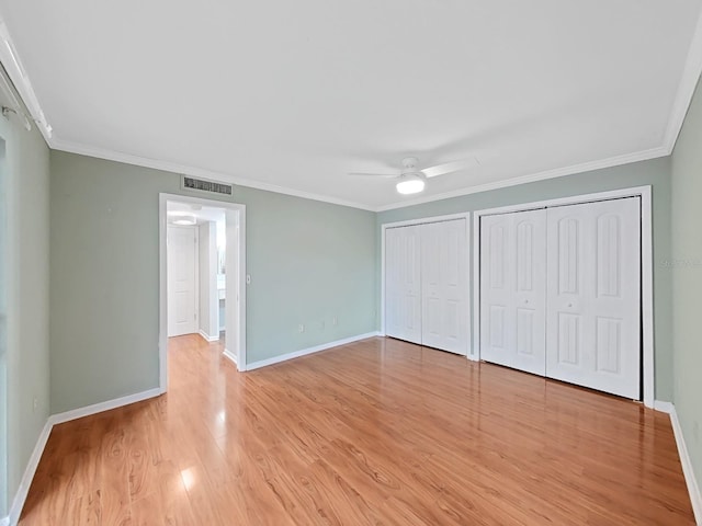 unfurnished bedroom with visible vents, light wood-type flooring, baseboards, two closets, and ornamental molding