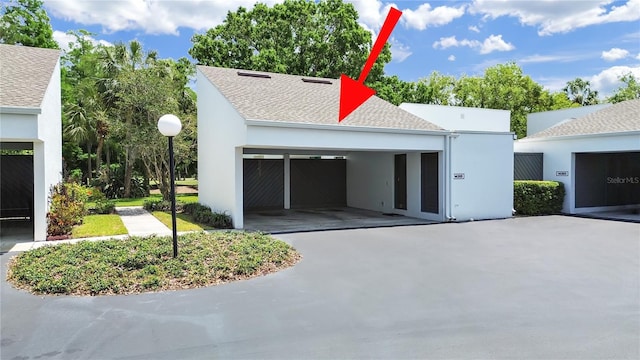 exterior space with a garage, a shingled roof, and stucco siding