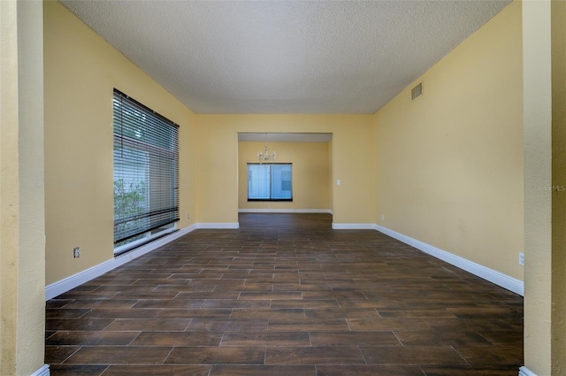 empty room featuring an inviting chandelier, a textured ceiling, baseboards, wood finished floors, and visible vents