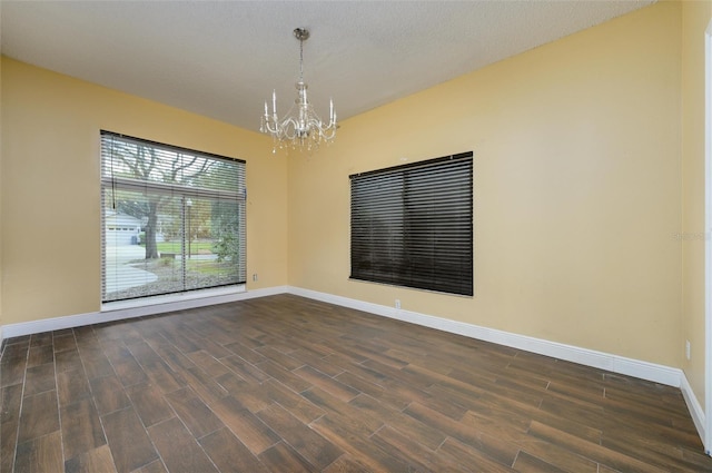 spare room with baseboards, an inviting chandelier, and dark wood-type flooring