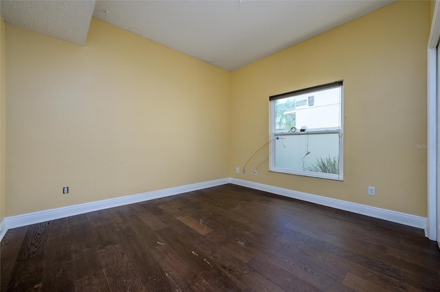 spare room with baseboards and dark wood finished floors