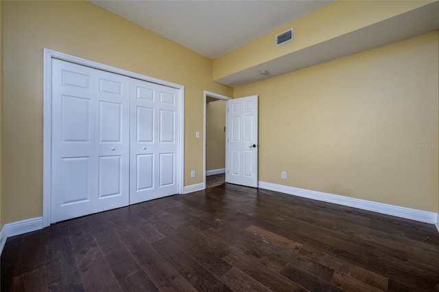 unfurnished bedroom with baseboards, a closet, dark wood finished floors, and visible vents