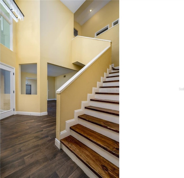 stairs with recessed lighting, baseboards, wood finished floors, and a high ceiling