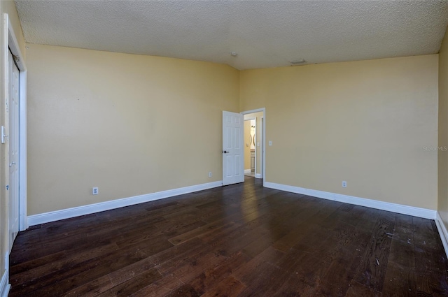 spare room featuring a textured ceiling, baseboards, dark wood finished floors, and vaulted ceiling