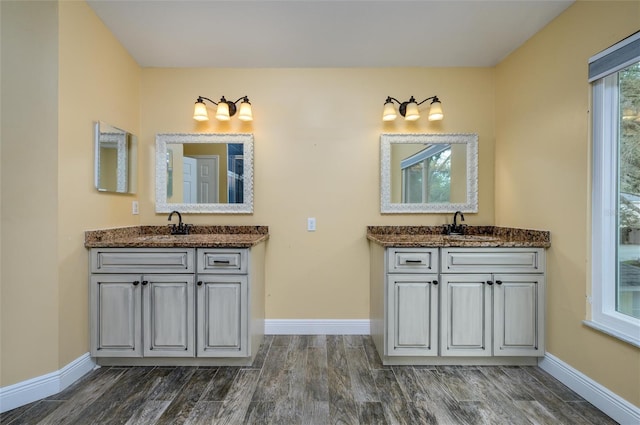 full bath featuring baseboards, a sink, two vanities, and wood finished floors