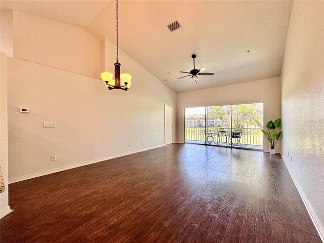 spare room featuring ceiling fan with notable chandelier, baseboards, vaulted ceiling, visible vents, and dark wood-style floors