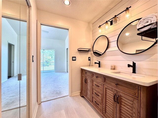 full bathroom with a sink, a textured ceiling, double vanity, and wood finished floors