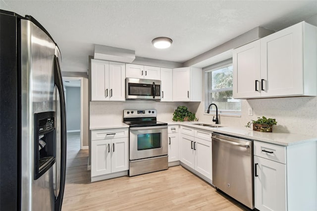 4940 Rosedale Ln, Holiday, FL 34690 - kitchen featuring appliances with stainless steel finishes, a sink, light countertops, white cabinets, and light wood-style flooring