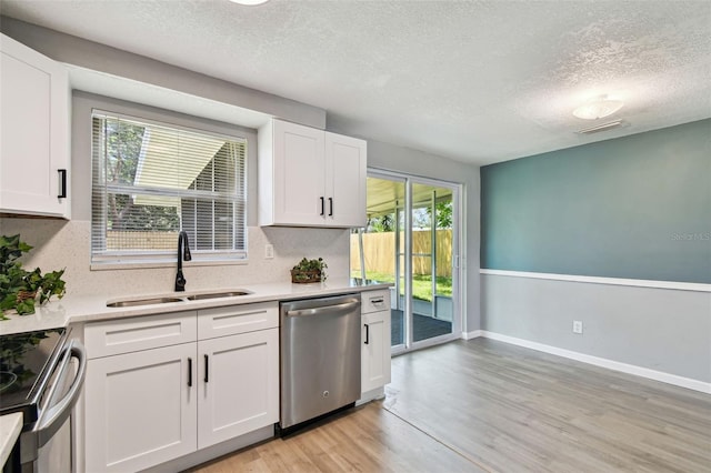 4940 Rosedale Ln, Holiday, FL 34690 - kitchen with light wood-style floors, a textured ceiling, white cabinetry, a sink, and appliances with stainless steel finishes