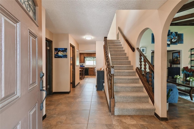 foyer with stairway, a textured ceiling, baseboards, and arched walkways