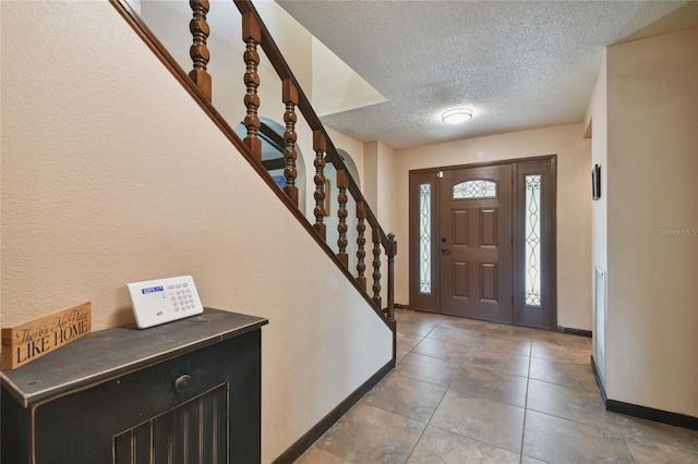 tiled foyer entrance with a textured ceiling, stairway, and baseboards